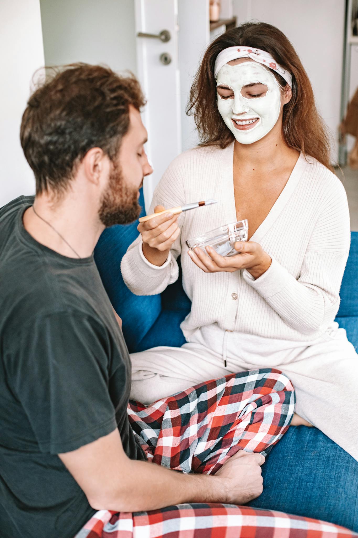A couple engaging in a skincare routine with facial cream and smiles, creating a cozy home atmosphere.
